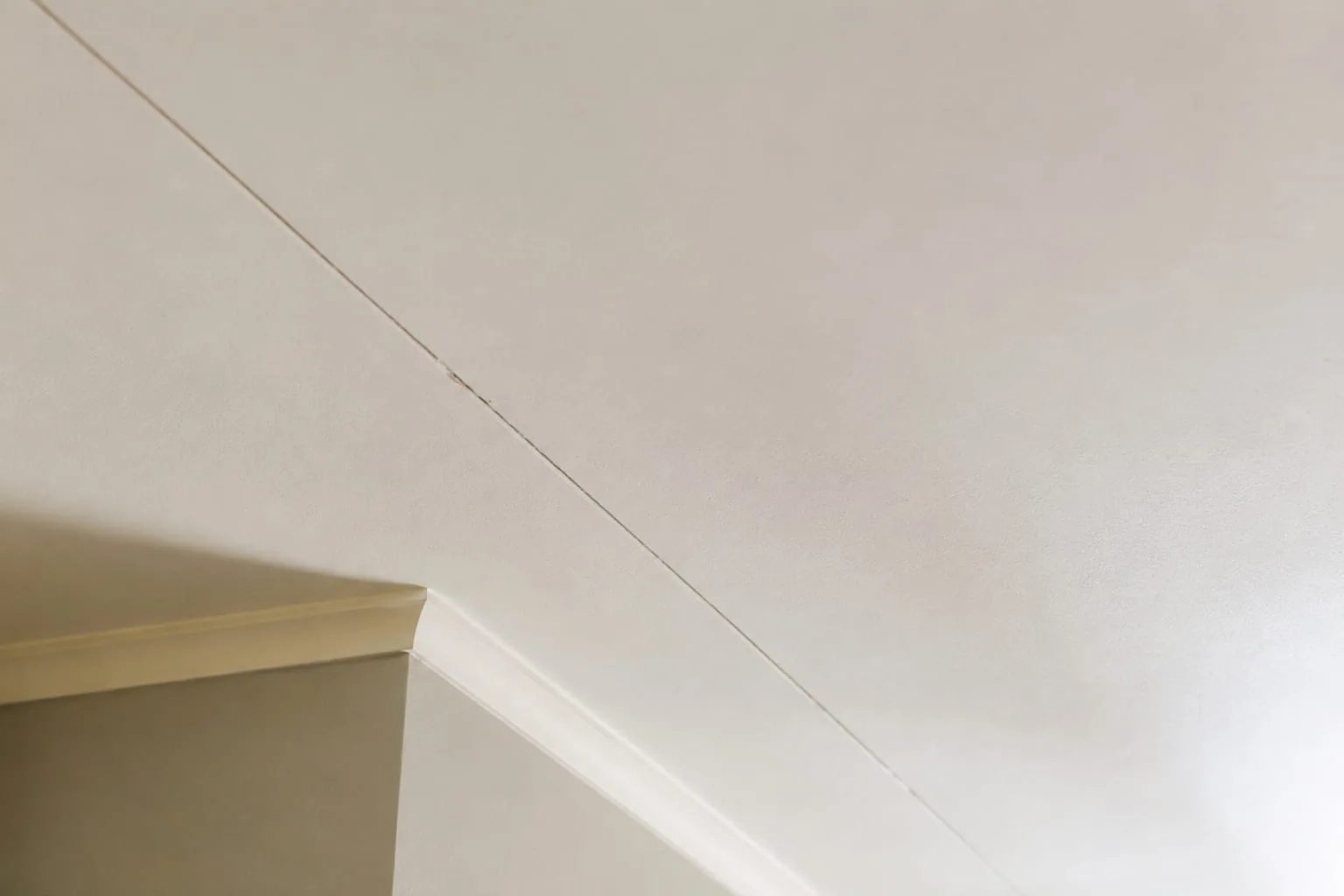 Hairline crack running along a plasterboard ceiling sheet join in a Perth residential interior, showing the thin straight line typical of cosmetic cracking rather than structural failure.