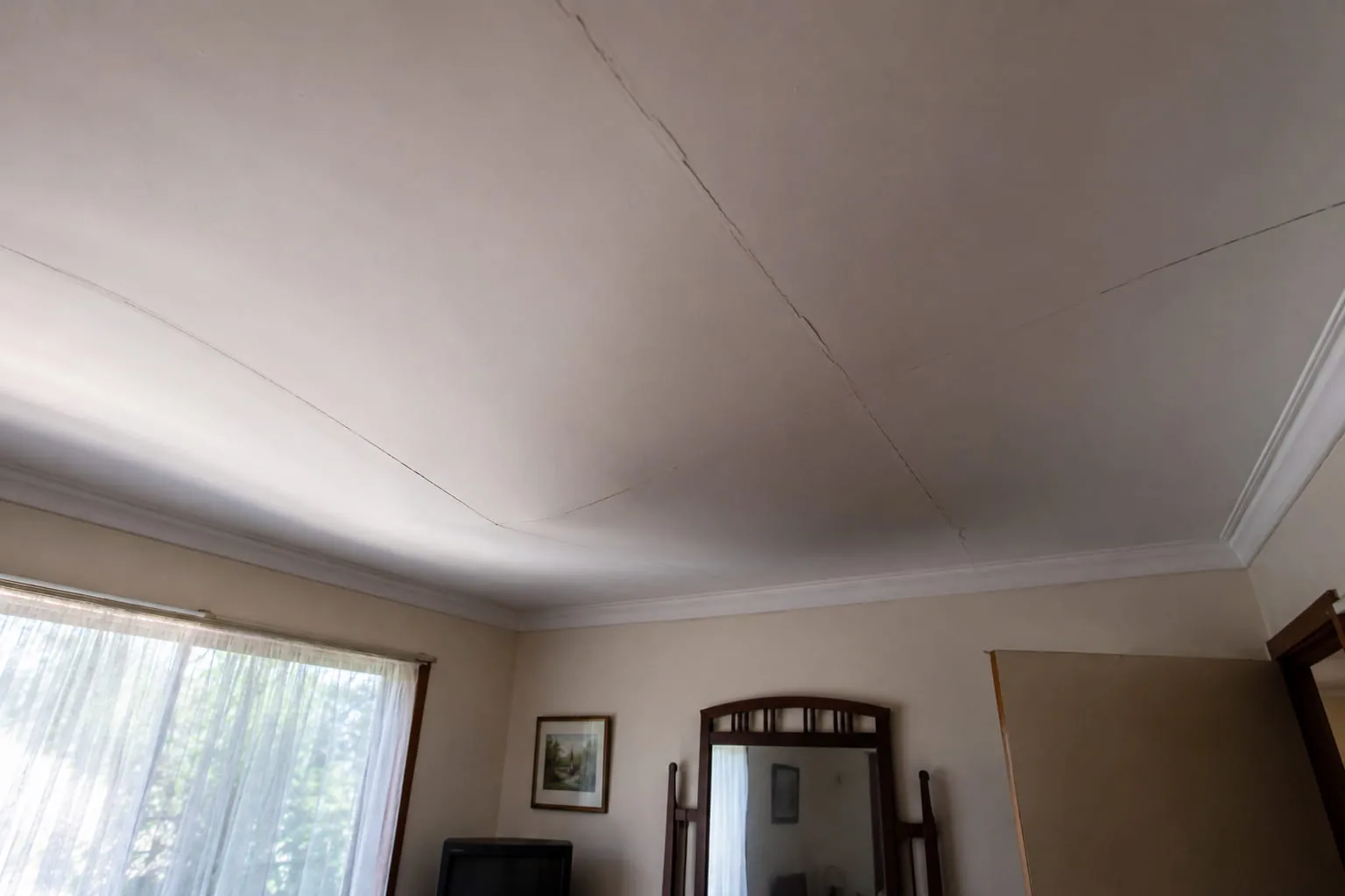 Sagging plasterglass ceiling in an older Perth home viewed from across the room, showing visible bow, cracks along sheet joins, and developing failure typical of mid-stage sagging.